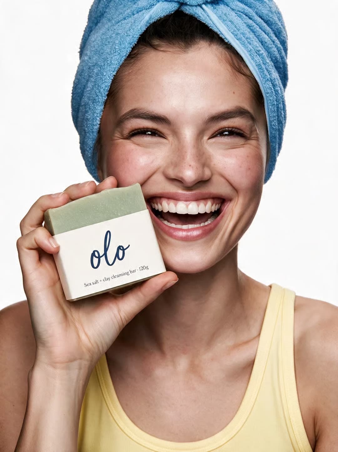 A smiling woman in a towel holds a bar of Olo soap to camera
